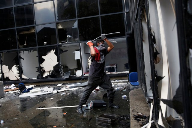 An anti-government protester breaks the windows of a public building in Caracas
