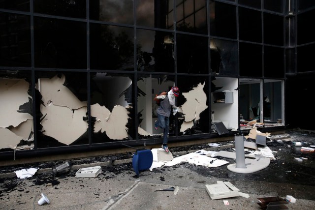A anti-government protester jumps out of a broken window while looting a public building in Caracas