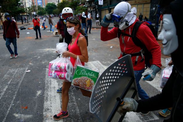 Anti-government protesters escort a woman carrying goods from the supermarket during riots with police in Caracas