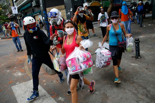 Anti-government protesters escort women carrying goods from the supermarket during riots with police in Caracas