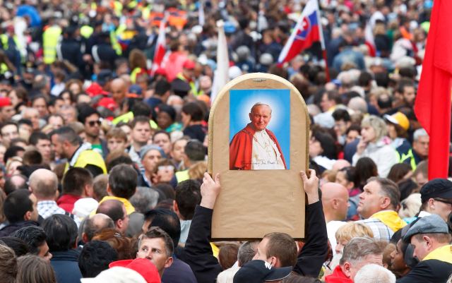 A Catholic faithful raises an image of Pope John Paul II through the crowds waiting to attend the canonisation ceremony of Popes John XXIII and John Paul II at the Vatican