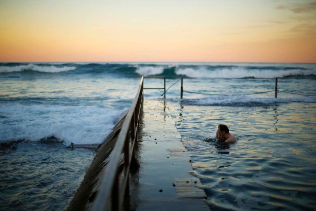 Un nadador salpica su rostro entre las vueltas en una piscina como las olas del rollo Océano Pacífico en durante el crepúsculo en South Cronulla Beach de Sydney