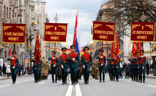 Sirviendo a los oficiales del ejército ruso que transportaba las normas de regimiento y entusiastas que usan la Segunda Guerra Mundial los uniformes militares soviéticos marchan durante un desfile en San Petersburgo 