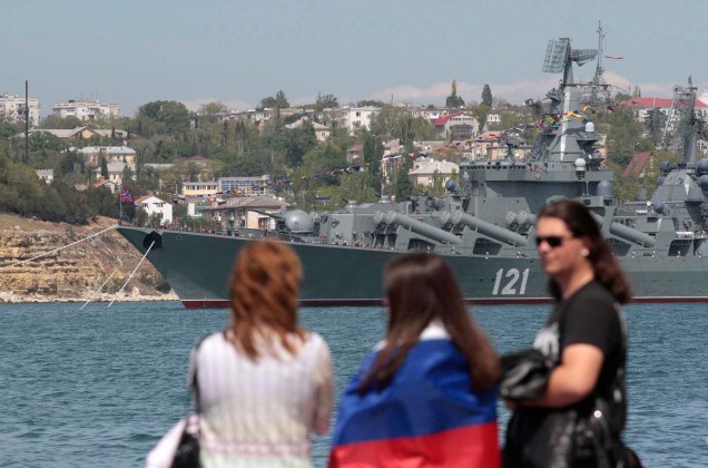 La gente camina a lo largo de un muelle como un buque de la Armada rusa está anclado en una bahía del puerto del Mar Negro de Sebastopol en Crimea / Stringer  / Reuters