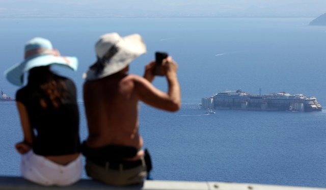 A woman takes a picture of Costa Concordia after it left Giglio Island