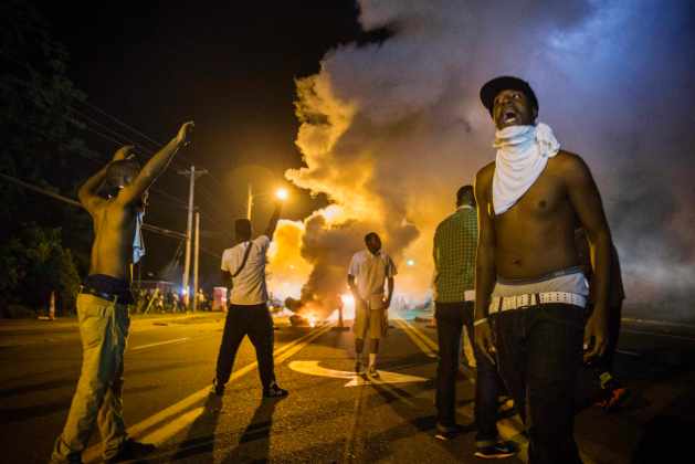 Demonstrators stand in the middle of West Florissant as they react to tear gas fired by police during ongoing protests in reaction to the shooting of Brown, in Ferguson