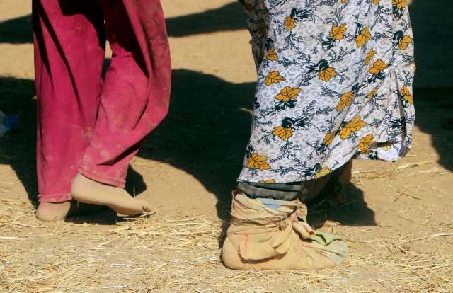 A displaced woman from the minority Yazidi sect, fleeing violence from forces loyal to the Islamic State in Sinjar town, covers her feet with clothes as she walks with others towards the Syrian border, on the outskirts of Sinjar mountain, near the Syrian b