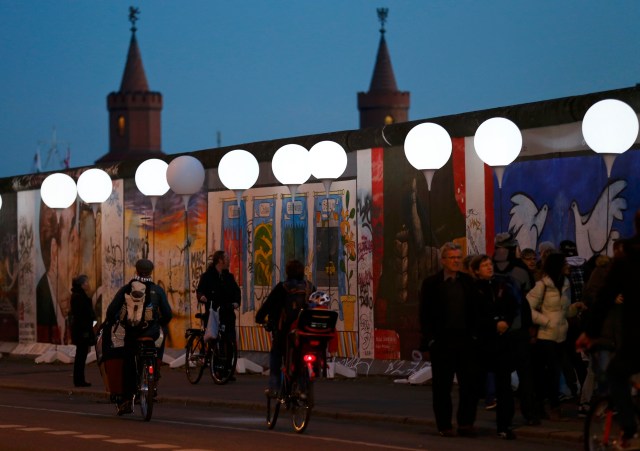 People walk under stands with balloons placed along the former Berlin Wall location at East Side Gallery, in Berlin