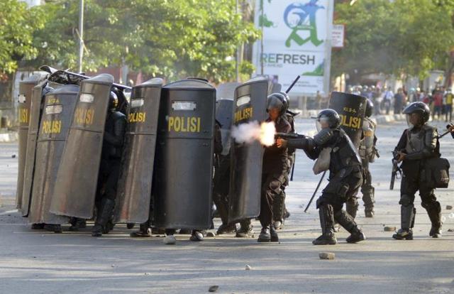 Un agente de policía indonesio dispara gas lacrimógeno a unos manifestantes mientras el resto de oficiales se protege durante un enfrentamiento en Makassar, al sur de las islas de Sulawesi. (Foto EFE/STR)