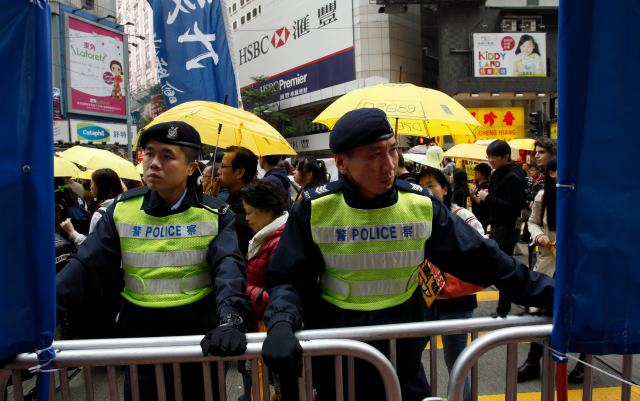 Policemen guard fences as protesters march past them carrying yellow umbrellas, the symbol of the Occupy movement, during a march in Hong Kong