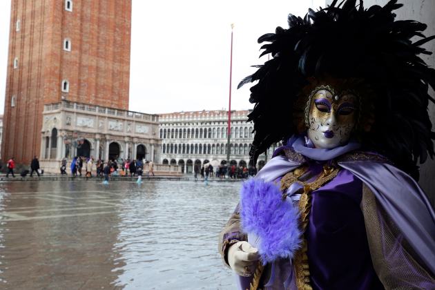 A masked reveller poses along the flooded St. Mark's Square during a period of seasonal high water and on the first day of carnival, in Venice