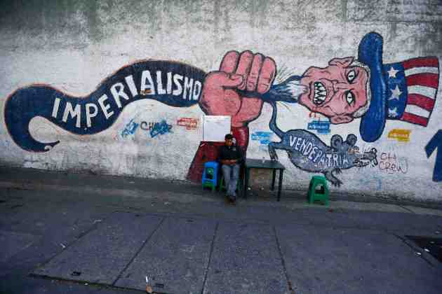 A man sits next to graffti, which reads "imperialism" and "traitor", in Caracas