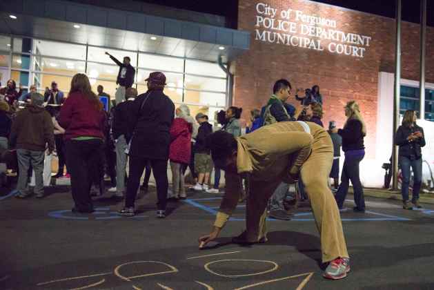 Protesters write slogans in chalk outside the City of Ferguson Police Department and Municipal Court in Ferguson