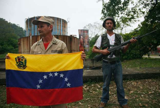 A militia member holds a national Venezuelan flag next to a worker of the national electricity company (CORPOELEC), as they pose for the media during a defensive military exercise in a thermoelectric power plant in La Fria
