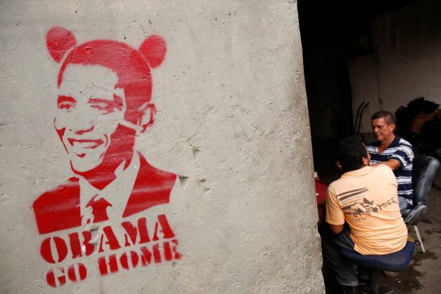 People sit next to graffiti depicting U.S. President Barack Obama in Caracas