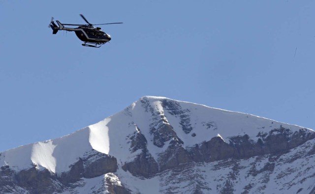 A rescue helicopter from the French Gendarmerie flies over the snow covered French Alps during operations near the crash site of the Germanwings Airbus A320