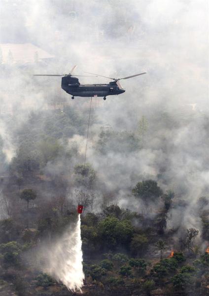 Un helicóptero "Chinook" de la Fuerza Aérea singapurense vierte agua sobre una zona boscosa en llamas en una montaña en la provincia de Chiang Mai, en el norte de Tailandia, hoy, jueves 19 de marzo de 2015. Singapur envió dos helicópteros a Tailandia para ayudar en las labores de extinción de un incendio declarado en el norte del país. Varias provincias septentrionales tailandesas se han visto afectadas por la cortina de humo causada por el incendio descontrolado de campos y de bosques. EF/EPongmanat Tasiri
