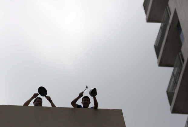 People bang pots from a rooftop at the same time while Venezuela's President Nicolas Maduro addresses the audience at the first plenary session of the VII Summit of the Americas in Panama City