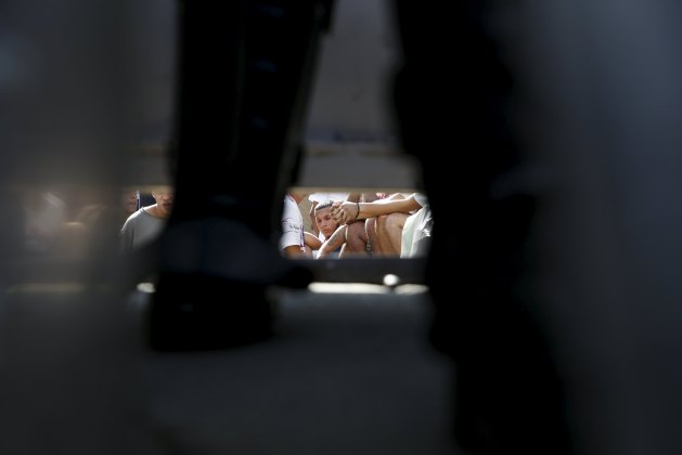 Inmates are seen sitting down, under a gate and through the legs of a police officer at the National Bolivarian Police prison, during a riot in Caracas, Venezuela