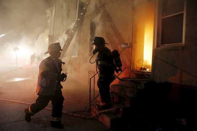 Baltimore firefighters confer as they attack a fire set by rioters in a convenience store and residence at East Biddle Street and Montford Avenue during rioting in Baltimore