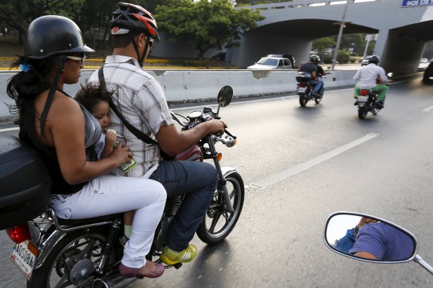 A girl drinks juice on a motorcycle while being driven on a highway in Caracas