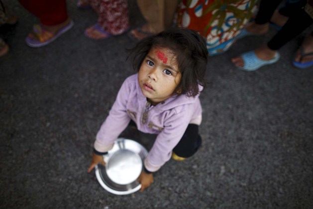 Girl holding her plate sits near the queue to receive food, near a makeshift shelter after the April 25 earthquake in Kathmandu