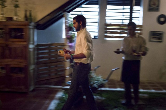Emiliano, owner of the restaurant "Ciboulette Prive" and a waiter carry dishes for diners in Caracas