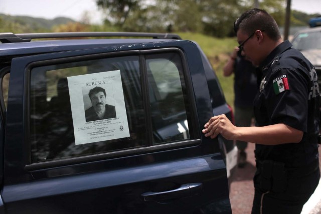 A Federal Police officer opens the door of one of their cars with a picture of fugitive drug lord Joaquin "El Chapo" Guzman's at a checkpoint on the highway connecting Mexico City and Acapulco, in Guerrero State, Mexico, on July 14, 2015. Mexico's government offered a $3.8 million reward for the capture of "El Chapo" Guzman on Monday and sacked top prison officials amid suspicions that guards helped him escape. Guzman vanished from his cell late Saturday even though he was wearing a monitoring bracelet and surveillance cameras were trained on the room 24 hours a day, Interior Minister Miguel Angel Osorio Chong said.  AFP PHOTO / PEDRO PARDO