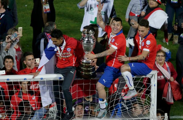 Chile players Vargas and Medel climb atop the goal with the Copa America trophy as they celebrate their team's victory over Argentina in their Copa America 2015 final soccer match at the National Stadium in Santiago