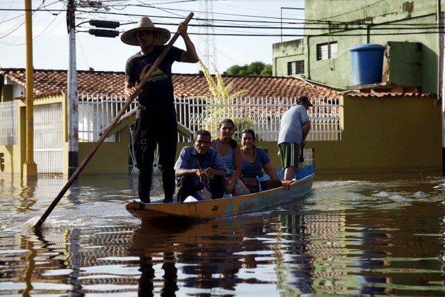 People sit in a boat in a flooded street in Guasdualito, in the state of Apure