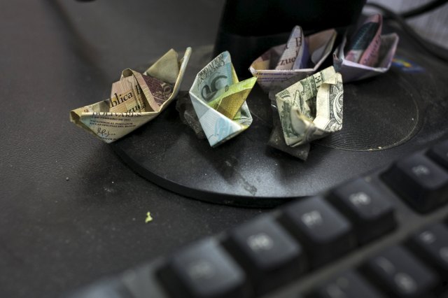 Venezuelan bolivar banknotes and a U.S. dollar banknote, folded as boats, are seen at a fruit and vegetable store in Caracas July 10, 2015. Origami-like boats made from Venezuela's rapidly depreciating bolivar bills sit on the cash register of the small fruit and vegetable store in Caracas. Cashier Marisol Garcia makes the bolivar boats to illustrate roaring inflation and the currency's tumble on the black market, where even the country's biggest bill is worth just 16 U.S. cents. REUTERS/Marco Bello