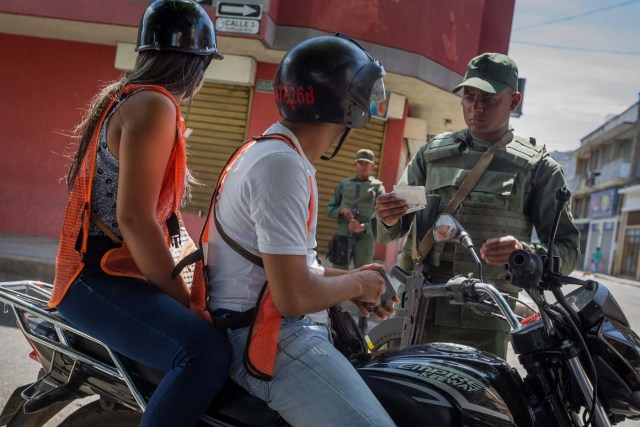 CAR08. SAN ANTONIO (VENEZUELA), 30/08/2015.- Un integrante del ejército venezolano inspecciona a un motociclista en las inmediaciones de la Aduana Principal fronteriza entre Colombia y Venezuela hoy, domingo 30 de agosto de 2015, en la ciudad de San Antonio (Venezuela). El Gobierno de Venezuela reiteró hoy que el cierre de parte de la frontera solo ha generado beneficios a su país después de que las autoridades hicieran un recorrido para confirmar que la medida se está cumpliendo en 140 kilómetros de los límites con Colombia. El presidente de Venezuela Nicolás Maduro decidió cerrar parte de la frontera con Colombia la medianoche del 19 de agosto después de que tres militares y un civil venezolanos resultasen heridos en un ataque de supuestos contrabandistas en la zona limítrofe a lo que sumó, dos días después, el decreto de estado de excepción en la zona. EFE/MIGUEL GUTIÉRREZ