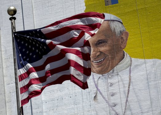 The U.S. flag flies in front of a mural of Pope Francis on the side of a building in midtown Manhattan in New York