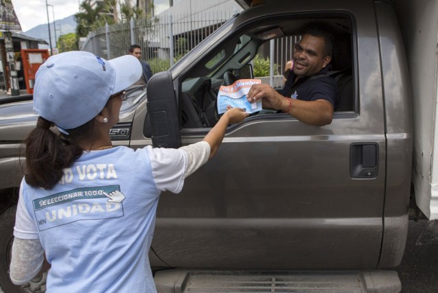 A driver receives a flyer from a supporter of MIN Unidad Party with information on how to vote in Caracas