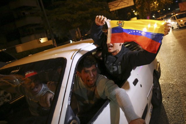 REFILE - ADDING NAME OF OPPOSITION Supporters of the opposition Democratic Unity coalition wave a Venezuelan national flag from a car while they celebrate their victory on a street in Caracas December 7, 2015. Venezuela's opposition won control of the legislature from the ruling Socialists for the first time in 16 years on Sunday, giving them a long-sought platform to challenge President Nicolas Maduro. REUTERS/Nacho Doce