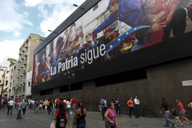 People walk past a billboard depicting Venezuela's President Nicolas Maduro and Venezuela's late President Hugo Chavez and the words "The country continues" in Caracas December 10, 2015. REUTERS/Christian Veron