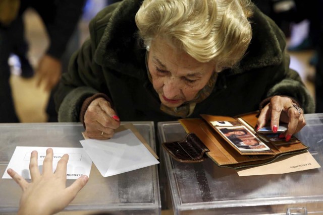 A woman looks down to check her name on the list at a polling official before voting in Spain's general election in Pozuelo de Alarcon, near Madrid, Spain, December 20, 2015. REUTERS/Susana Vera