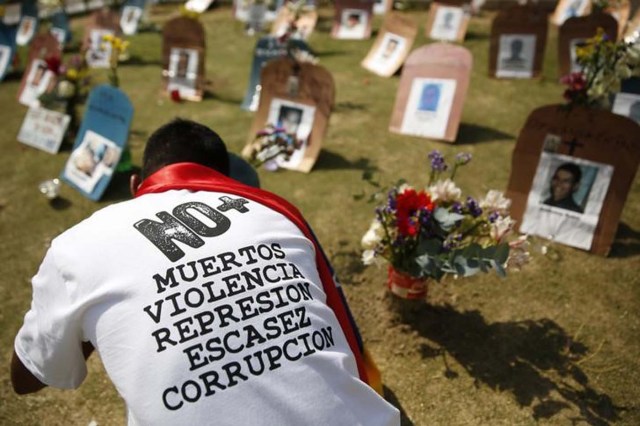 Una persona pone velas frente a unas simulaciones de tumbas con fotografías de víctimas de violencia, durante una protesta contra el gobierno de Nicolás Maduro, en Caracas, 10 de abril de 2014. Las muertes violentas en Venezuela llegarían a 27.875 este año, un aumento del 12 por ciento respecto del anterior, según un estudio presentado el lunes por la organización no gubernamental Observatorio Venezolano de Violencia (OVV). REUTERS/Carlos Garcia Rawlins