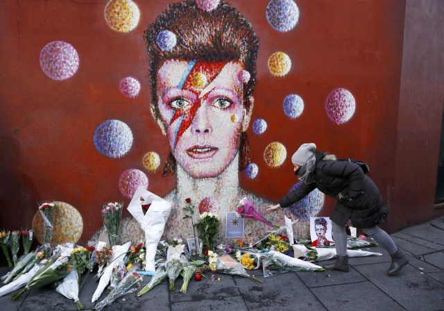 A woman leaves a bouquet at a mural of David Bowie in Brixton, south London, January 11, 2016. David Bowie, a music legend who used daringly androgynous displays of sexuality and glittering costumes to frame legendary rock hits "Ziggy Stardust" and "Space Oddity", has died of cancer. REUTERS/Stefan Wermuth