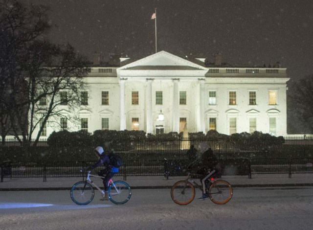 Two people bike through the snow past the White House in Washington, DC on January 20, 2016. / AFP / Andrew Caballero-Reynolds