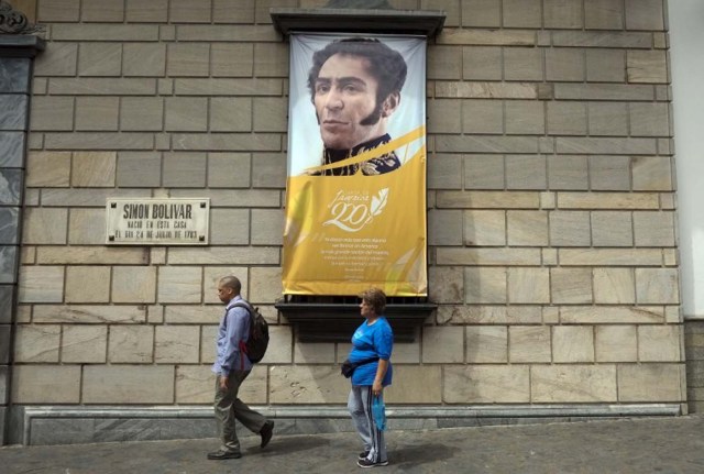 People walk past a banner of Venezuelan independence hero Simon Bolivar in downtown Caracas in January 27, 2016. The economic debacle of Venezuela deepens as oil prices are bottoming out.  AFP  PHOTO/JUAN BARRETO / AFP / JUAN BARRETO