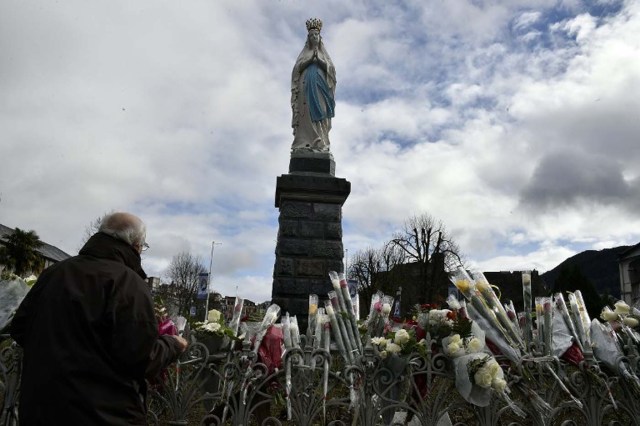 A pilgrim puts flowers in front of a statue of Virgin Mary inside in the sanctuary of Lourdes, southern France on February 11, 2016 for the 158th anniversary of the virgin Mary's apparition to Bernadette Soubirous. / AFP / PASCAL PAVANI