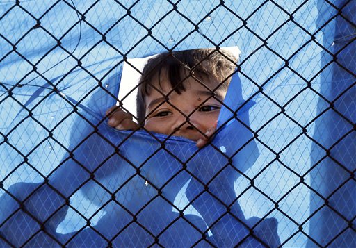 Un niño migrante mira a través de un agujero en una malla en la verja de un campo de refugiados en el suburbio de Schisto, en Atenas, el 4 de abril de 2016, el día en que entró en vigor el acuerdo migratorio entre la UE y Turquía. (Foto AP/Lefteris Pitarakis)