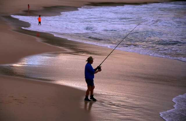 Un pescador se encuentra en el borde de las olas después de emitir su línea al atardecer en la playa de Bronte de Sydney, Australia, 11 de julio de 2016. REUTERS / David Gray
