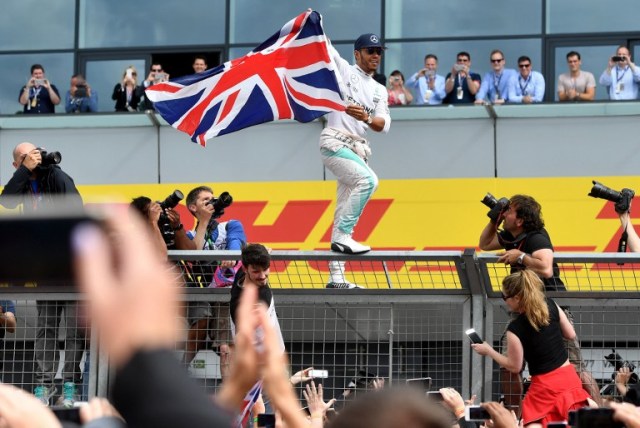 Mercedes AMG Petronas F1 Team's British driver Lewis Hamilton celebrates with fans after climbing the paddock fence after winning the British Formula One Grand Prix at Silverstone motor racing circuit in Silverstone, central England, on July 10, 2016. Lewis Hamilton streaked away to comfortably win his home British Grand Prix on Sunday, with Mercedes team-mate Nico Rosberg hanging on for a provisional second. Third was the Red Bull of Max Verstappen, but championship leader Rosberg -- suffering late gear-box trouble -- was under investigation over a radio communication that could spell further trouble for the German. / AFP PHOTO / ANDREJ ISAKOVIC