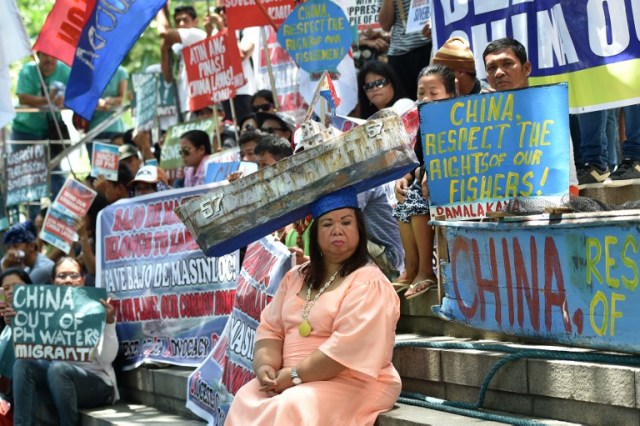 An activist wearing a hat representing the Philippine navy boat "Sierra Madre", now half-submerged at Second Thomas shoal of the Spratly islands, sits with protesters during a demonstration in front of the Chinese consulate in Manila on July 12, 2016, ahead of a UN tribunal ruling on the legality of China's claims to an area of the South China sea contested by the Philippines. Beijing lays claim to virtually all of the South China Sea, putting it at odds with regional neighbours the Philippines, Vietnam, Malaysia, Brunei and Taiwan, which also have partial claims. / AFP PHOTO / TED ALJIBE