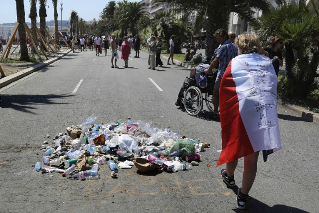 La gente tira la basura el 18 de julio de 2016 el paseo marítimo Promenade des Anglais en Niza, en el sitio donde Mohamed Lahouaiej-Bouhlel, un tunecino de 31 años de edad que conducía un camión contra una multitud de ver un espectáculo de fuegos artificiales en el Día de la Bastilla, murió por la policía. El mensaje dice "cobarde". Francia fue creada para mantener un minuto de silencio el 18 de julio de 2016 para cumplir con las 84 víctimas del ataque camión agradable, pero un período de duelo nacional se vio ensombrecida por disputas / AFP
