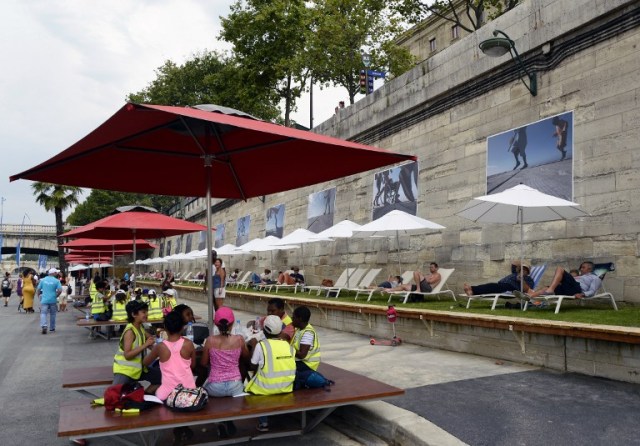 People sit around a table as others relax on deckchairs in "Paris Plage" (Paris Beach) during the opening day of the event on the bank of the Seine river, in central Paris, on July 20, 2016. The 15th edition of Paris Plage will run until September 4, 2016. / AFP PHOTO / BERTRAND GUAY