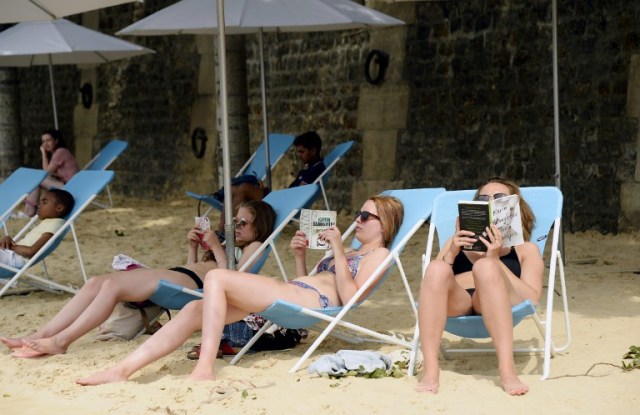 Women read as they sunbath in "Paris Plage" (Paris Beach) during the opening day of the event on the bank of the Seine river, in central Paris, on July 20, 2016. The 15th edition of Paris Plage will run until September 4, 2016. / AFP PHOTO / BERTRAND GUAY