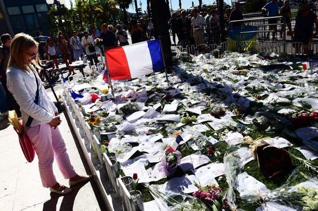 A woman reacts as people gather around the makeshift memorial where flowers, candles and messages were laid in Nice on July 16, 2016, in tribute to the victims of the deadly attack on the Promenade des Anglais seafront which killed 84 people. The Islamic State group claimed responsibility on July 16, 2016 for an attack in which a Tunisian drove a truck through a crowd in Nice, killing 84, prompting hard questions in France over security failures. / AFP PHOTO / GIUSEPPE CACACE